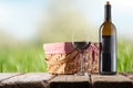 Close-up view of picnic basket with red wine bottle and wine glass stands on wooden rustic table on green garden background. Royalty Free Stock Photo