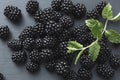 Close-up view on pile of glossy and tasty blackberries and green leaves laying on grey table