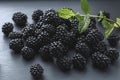 Close-up view on pile of glossy and tasty blackberries and green leaves laying on grey table