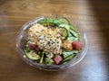 Close up view of a plastic bowl of salmon and tuna poke with crab salad, cucumbers, and avocado on a wooden table