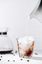 close up view of pouring milk into glass of cold brewed coffee process, coffee maker and roasted coffee beans Royalty Free Stock Photo