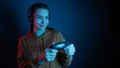 Close-up view of pretty woman with joystick and headphones playing video game in dark room on dark blue background. Gamer concept