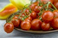 Close up view of red cherry tomatoes bunch in a plate and yellow sweet pepper on light background Royalty Free Stock Photo