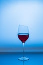 Close up view of red wine being poured into graceful slim wine glass isolated on blue background. Royalty Free Stock Photo