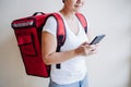 Close up view of rider woman wearing red backpack delivering food, checking order with smart phone while standing on street in Royalty Free Stock Photo