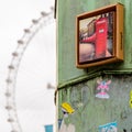 Close up view of a rusty metal column with stickers and a red phone booth photo on it with the London Eye on the background. Royalty Free Stock Photo