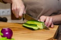 Close-up view of the salad preparation process. A woman in an apron cuts a cucumber on a wooden cutting board Royalty Free Stock Photo