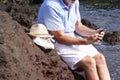 Close-up view of a senior bearded man using smart phone sitting on the rocks with feet into the fresh water enjoying the vacation Royalty Free Stock Photo