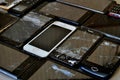 Close-up view of several cell phones of different colors and sizes with broken screens, push-button and touchscreens