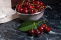 Several red sweet cherries and big green leaf on the table. Fresh organic cherry in colander on dark marble background.. Royalty Free Stock Photo
