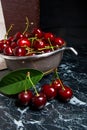 Several red sweet cherries and big green leaf on the table. Fresh organic cherry in colander on dark marble background.. Royalty Free Stock Photo