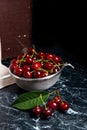 Several red sweet cherries and big green leaf on the table. Fresh organic cherry in colander on dark marble background.. Royalty Free Stock Photo