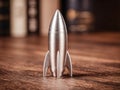 Close-up view of a shiny silver metal rocket model on a wooden surface with blurred background featuring vertical elements and Royalty Free Stock Photo