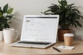 Close up view of simple workspace with laptop, notebooks, coffee cup and tree pot on white table with blurred office room backgrou
