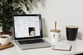 Close up view of simple workspace with laptop, notebooks, coffee cup and tree pot on white table with blurred office room backgrou