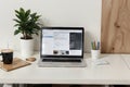 Close up view of simple workspace with laptop, notebooks, coffee cup and tree pot on white table with blurred office room backgrou