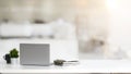 Close up view of simple workspace with laptop, notebooks, coffee cup and tree pot on white table with blurred office room