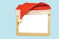 Close up view of small white mockup image blank board with red Santa hat over top isolated on blue background. Royalty Free Stock Photo