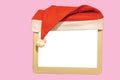 Close up view of small white mockup image blank board with red Santa hat over top isolated on pink background. Royalty Free Stock Photo