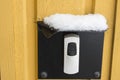Close up view of snowy protected cover over electric doorbell button .