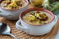 Close up view of a soup crock filled with chicken and corn chowder topped with grilled corn, ready for eating.