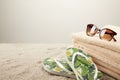 close up view of stack of towels, sunglasses and summer flip flops on sand on grey backdrop