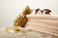 close up view of stack of towels, sunglasses, tanning oil and golden decorative pineapple on sand on grey backdrop