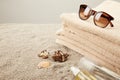 close up view of stack of towels, sunglasses, tanning oil and seashells on sand on grey background