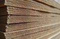 Close-up view of stacked corrugated cardboard sheets. Material texture is visible. Sheets are neatly arranged in a large stack.