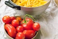 Close up view of a strainer full of Italian pasta and a cup full of tomatoes on a paper