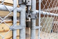 Close-up view of sturdy metallic padlock - chain-link fence gate - rusted metal barrels in background - industrial storage area Royalty Free Stock Photo