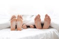 Family of three hiding under blanket with bare feet outside