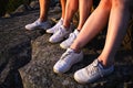 Close up view of three pairs of legs in white sneakers in nature at sunset
