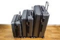 Close-up view of three suitcases of different sizes with extended handles, standing on parquet floor in room.