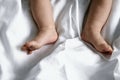 Close-up view of the top bare feet of newborn baby on white bed linen with space for text Royalty Free Stock Photo