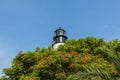 Close up view of top of lighthouse over green trees on blue sky background Royalty Free Stock Photo