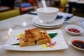 Close up view of traditional dim sum with sauces in foreground pan fried turnip cake plated with leaf and flower petals. Bowls Royalty Free Stock Photo