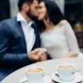 Close-up view of the two cups of coffee at the blurred background of the kissing newlyweds. Royalty Free Stock Photo