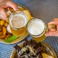 Two glass of beer in hand. Beer glasses clinking in bar or pub on table with food background Royalty Free Stock Photo