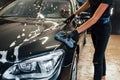 Close up view of vehicle getting wiped. Modern black automobile get cleaned by woman inside of car wash station Royalty Free Stock Photo