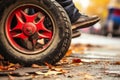 Close-up view of a vibrant red wheelchair rear wheel with persons feet on footplates in front of a picturesque autumn scene