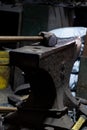 Close-up view of a vintage hammer resting on an anvil, set against a dimly lit workshop background, highlighting the textures and