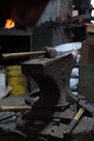Close-up view of a vintage hammer resting on an anvil, set against a dimly lit workshop background, highlighting the textures and