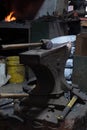 Close-up view of a vintage hammer resting on an anvil, set against a dimly lit workshop background, highlighting the textures and