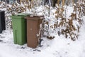 Close up view of waste and recycling containers against backdrop of snow-covered bushes in front of private villa.