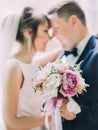 Close-up view of the wedding bouquet of the colourful peonies in the hands of the smiling newlyweds.