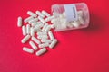 Close up view of white capsules spilling from a placebo bottle on a red background with space