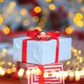 Close up view white gift with a red ribbon and small decoration toy red car. Present on background of xmas tree lights bokeh. Royalty Free Stock Photo