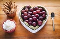 Close-up view of white heart-shaped plate full of red grapes, cream and biscuits. Wooden background