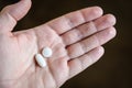 A white male hand holding two white pills in the palm against a dark background Royalty Free Stock Photo